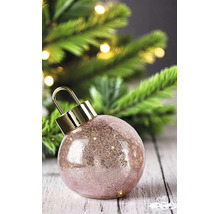 Boule de Noël en verre texturé rose avec un capuchon doré devant un sapin de Noël illuminé.