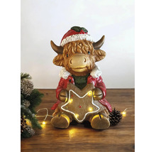 Figurine de Noël vache des Highlands avec bonnet et manteau tenant une étoile en pain d epice lumineuse.