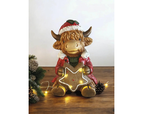 Figurine de Noël vache des Highlands avec bonnet et manteau tenant une étoile en pain d epice lumineuse.
