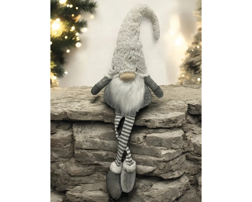 Dekorativer Weihnachtswichtel mit Paillettenmütze, weissem Bart und gestreiften Beinen sitzend auf einer Steinmauer.