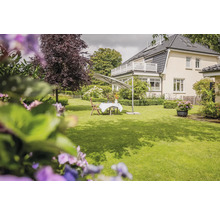 Un grand jardin avec pelouse, mobilier de jardin en bois et un grand parasol déporté gris devant une maison.