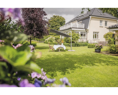 Moderner Ampelschirm über einem Gartentisch mit Stühlen auf einer gepflegten Rasenfläche vor einem Wohnhaus.