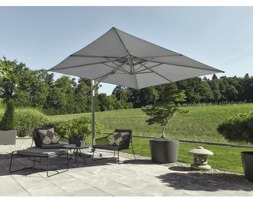 Moderner Aussenbereich mit grossem quadratischem Ampelschirm, Lounge-Sesseln und Beistelltisch auf einer hellen Steinterrasse mit Gartenblick.