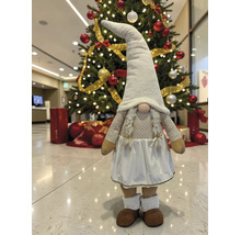 Dekorative Weihnachts-Wichtelfigur mit Zöpfen, langem Hut und Kleid vor einem geschmückten Weihnachtsbaum.
