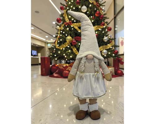 Dekorative Weihnachts-Wichtelfigur mit Zöpfen, langem Hut und Kleid vor einem geschmückten Weihnachtsbaum.
