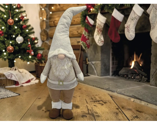 Weihnachts-Gnom Dekorationsfigur in einem festlichen Wohnzimmer mit geschmücktem Tannenbaum und brennendem Kamin.