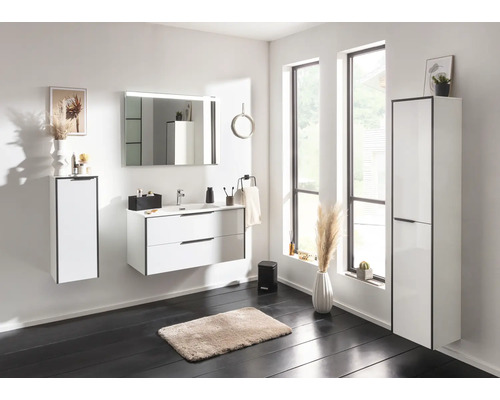 Salle de bains moderne et lumineuse avec meubles blancs, comprenant un sous-lavabo, un miroir avec éclairage et des armoires hautes.
