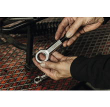 Hände halten einen Mutternsprenger aus Metall in einer Werkstatt über einem Gitterrost.