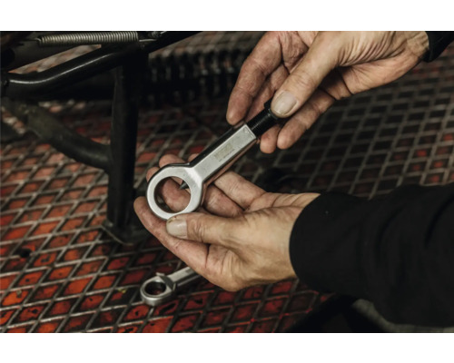 Hände halten einen Mutternsprenger aus Metall in einer Werkstatt über einem Gitterrost.