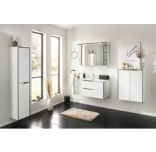 Ensemble de salle de bains moderne et lumineux avec meuble sous-lavabo blanc à deux tiroirs, armoire de toilette et colonne sur sol sombre.