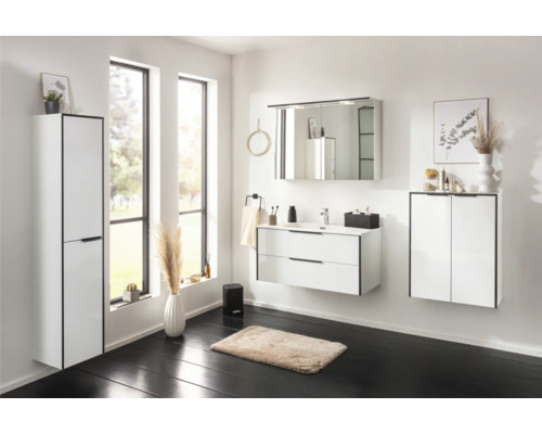 Ensemble de salle de bains moderne et lumineux avec meuble sous-lavabo blanc à deux tiroirs, armoire de toilette et colonne sur sol sombre.