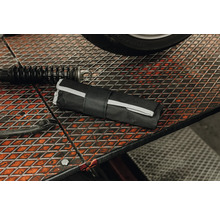 Trousse à outils noire enroulée sur un établi en grille métallique dans un atelier à côté d'un amortisseur.