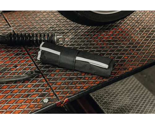 Trousse à outils noire enroulée sur un établi en grille métallique dans un atelier à côté d'un amortisseur.