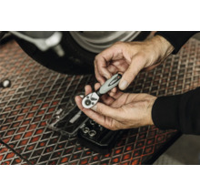 Mains tenant un cliquet pour embouts WGB au-dessus d'un établi dans un atelier à côté d'une moto.