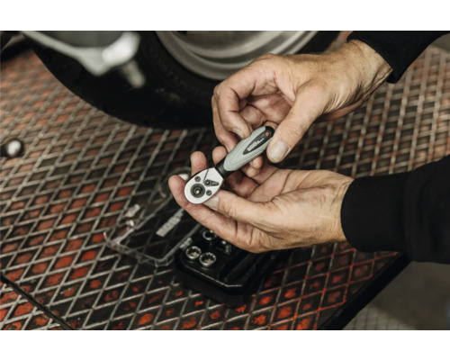 Mains tenant un cliquet pour embouts WGB au-dessus d'un établi dans un atelier à côté d'une moto.