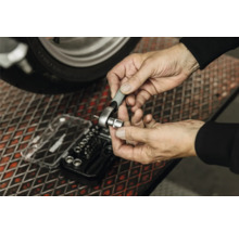 Une personne fixe une douille sur un petit cliquet au-dessus d'un coffret de douilles sur une grille métallique.