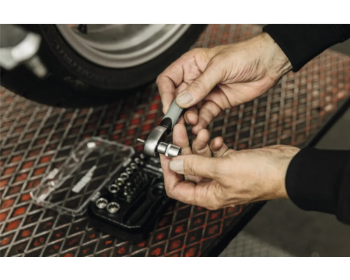 Une personne fixe une douille sur un petit cliquet au-dessus d'un coffret de douilles sur une grille métallique.