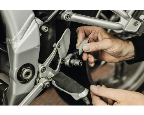 Personne utilisant un petit cliquet avec une douille pour l'entretien du cadre d'une moto.