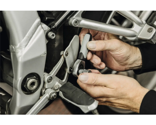 Mains utilisant un petit cliquet avec douille pour une réparation sur une moto.