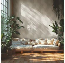 Helles Wohnzimmer mit Vliestapete im Palmblattmuster, niedrigem Holzsofa mit Kissen, Zimmerpflanzen und Sonnenlicht auf dem Holzboden.