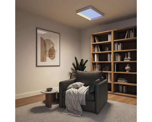 Quadratisches LED-Panel an der Decke eines modern eingerichteten Wohnzimmers mit grauem Sessel und Holzregal.