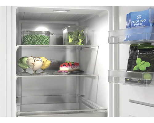 Vue intérieure d'un congélateur éclairé avec des clayettes en verre, des récipients contenant des légumes, de la glace, un gâteau et des balconnets.