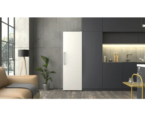 Réfrigérateur blanc posé librement dans une cuisine moderne et minimaliste avec façades sombres, mur en béton et sol en bois.