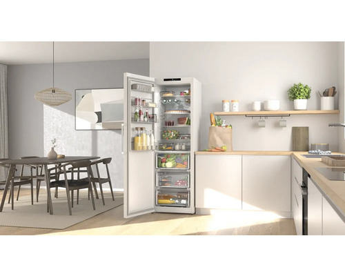 Moderne helle Küche mit offenem organisiertem Kühlschrank voller Lebensmittel und einem Essbereich mit Holztisch und Stühlen.