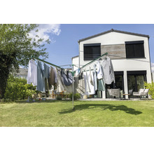 Séchoir parapluie en métal sur une pelouse devant une maison blanche moderne avec du linge. Jardin lumineux avec meubles de jardin à l'arrière.