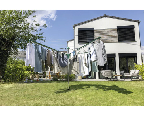 Séchoir parapluie en métal sur une pelouse devant une maison blanche moderne avec du linge. Jardin lumineux avec meubles de jardin à l'arrière.