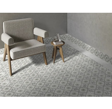 Pièce lumineuse avec des carreaux de sol à motifs et une bordure murale assortie, un fauteuil gris et une petite table d appoint en bois.