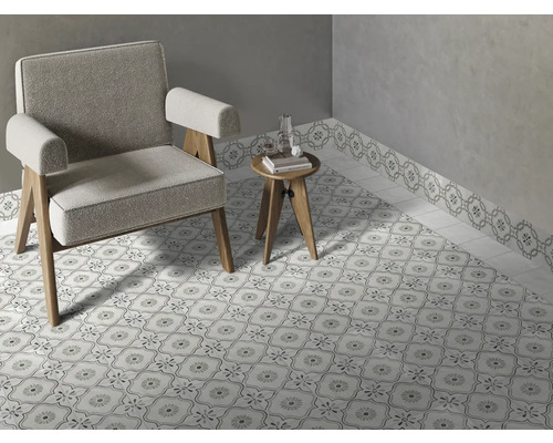 Pièce lumineuse avec des carreaux de sol à motifs et une bordure murale assortie, un fauteuil gris et une petite table d appoint en bois.