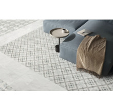 Hell gestalteter Wohnbereich mit dekorativ gemusterten Bodenfliesen, schlichten Fliesen im Randbereich und einem Sofa.