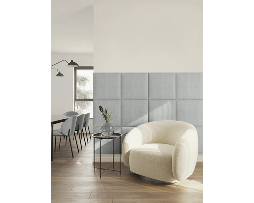Modernes, helles Wohnzimmer mit quadratischen, gepolsterten Wandpaneelen aus hellblauem Stoff neben einem runden Sessel aus weißem Bouclé-Stoff.