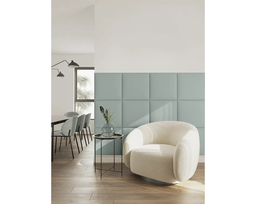 Modernes Wohnzimmer mit quadratischen Wandpaneelen, einem weißen Bouclé-Sessel, Beistelltisch mit Vase und Essbereich im Hintergrund.