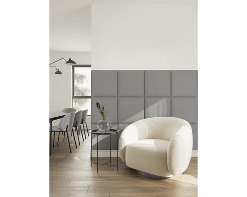 Modernes Wohnzimmer mit grauen quadratischen Polsterpaneelen an der Wand, einem weißen Sessel und einem Beistelltisch auf Holzboden.