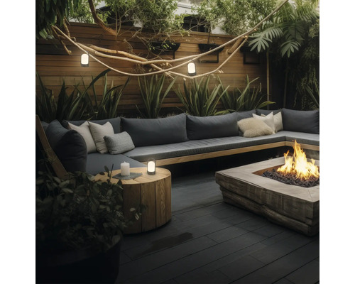 Espace salon extérieur moderne avec un grand banc en bois en forme de L, des coussins gris foncé et un foyer central sur une terrasse en bois sombre