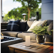 Lampe de table solaire d’extérieur moderne avec lumière chaude sur une table en bois dans un salon de jardin avec canapé et plante.