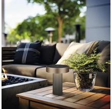 Lampe de table moderne sur une table en bois sur une terrasse de jardin lumineuse avec canapé, foyer et plante dans un pot en verre.