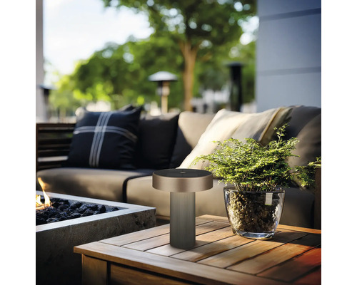 Lampe de table moderne sur une table en bois sur une terrasse de jardin lumineuse avec canapé, foyer et plante dans un pot en verre.