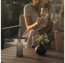 Lampe de table d'extérieur portable moderne sur une table en bois à côté d'un vase de fleurs dans une ambiance de soirée conviviale.