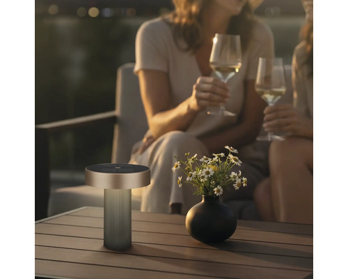 Lampe de table d'extérieur portable moderne sur une table en bois à côté d'un vase de fleurs dans une ambiance de soirée conviviale.