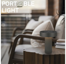 Lampe de table à LED portable moderne sur une table en bois dans un espace extérieur avec des fauteuils.