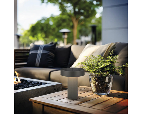 Lampe de table d'extérieur moderne sur une table en bois dans un salon de jardin organisé avec canapé, plante et foyer.