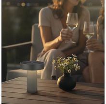 Lampe de table solaire LED moderne pour l'extérieur sur une table en bois dans une scène de jardin relaxante le soir.