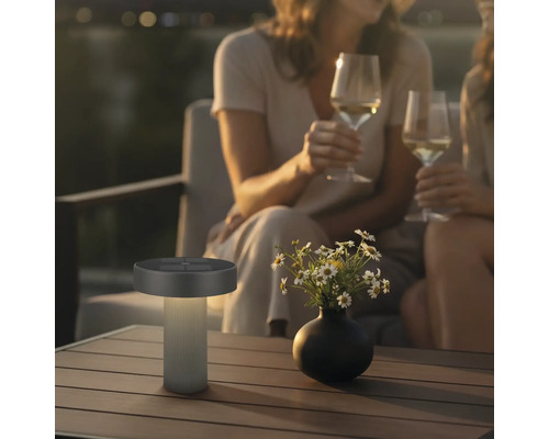 Lampe de table solaire LED moderne pour l'extérieur sur une table en bois dans une scène de jardin relaxante le soir.