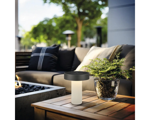 Lampe de table d'extérieur à LED moderne sur une table en bois dans un coin salon confortable avec foyer et plantes.