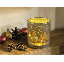 Zylindrisches Windlicht aus Glas mit beleuchtetem Rentier- und Waldmotiv, dekoriert mit Tannenzapfen auf einer Holzoberfläche.