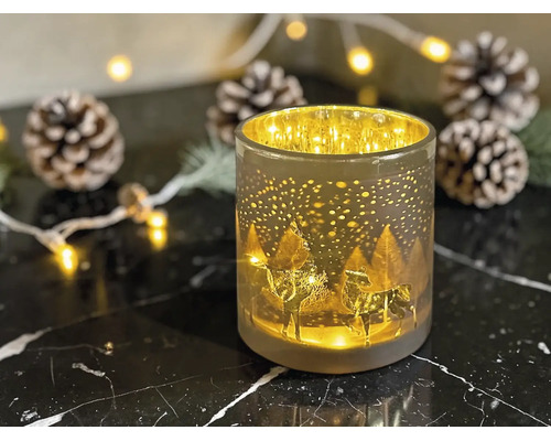 Windlicht aus Glas mit Hirsch-Motiv und Winterlandschaft, beleuchtet zwischen Weihnachtsdekoration wie Tannenzapfen.