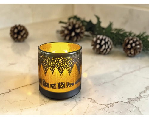 Windlicht aus Glas mit leuchtendem Wald-Silhouette-Muster auf Marmoroberfläche, dekoriert mit Tannenzapfen und Zweigen.